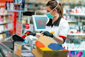 grocery cashier wearing protective face mask and gloves to prevent viruses, scanning disinfection products at the cash register. and packing in paper bag