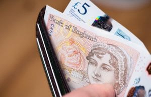 A black wallet held open with a finger revealing polymer British banknotes, a £10 note featuring the 19th Century author, Jane Austen is visible. 