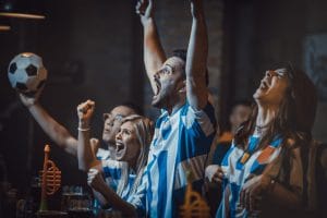 Group of excited soccer fans watching successful game on a TV in a bar